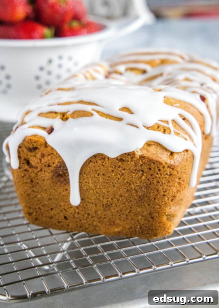 A close-up shot of the sweet almond glaze gracefully dripping down the golden-brown crust of the strawberry bread loaf.