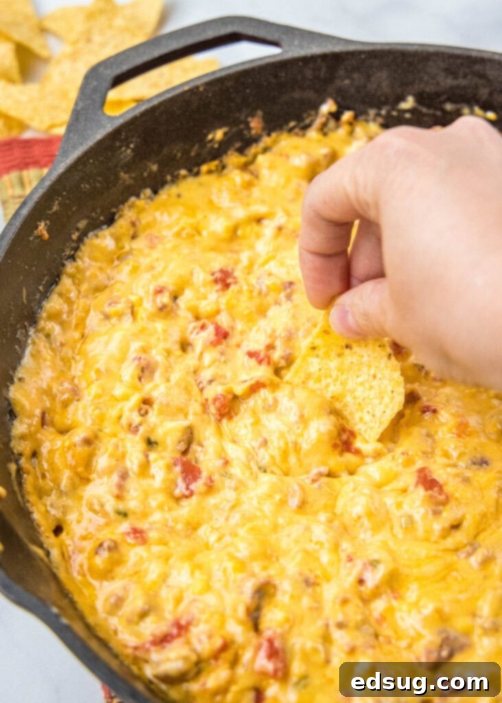 Dipping a tortilla chip into a hot, bubbly Smoked Queso dip, showing its thick and creamy texture.