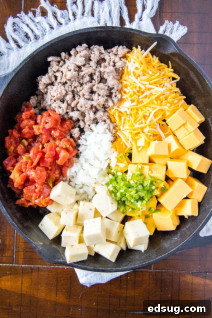 All the ingredients for Smoked Queso, including cubed Velveeta, sausage, diced vegetables, and shredded cheese, arranged in a cast iron skillet before smoking.