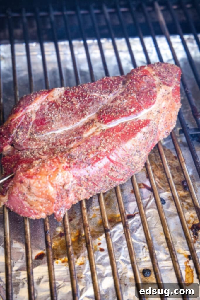 A beef chuck roast on the grates of a smoker, with visible smoke