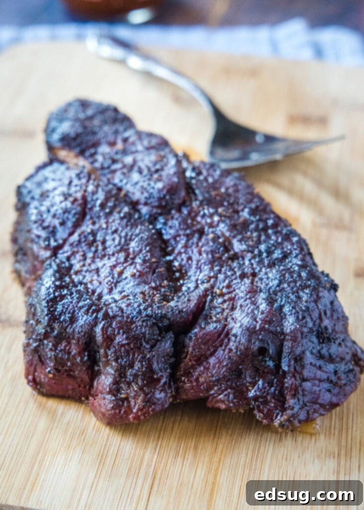 Whole smoked chuck roast on a wooden cutting board, with a dark, flavorful bark.