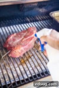 Spraying a chuck roast on the smoker with beef broth to keep it moist and enhance bark.