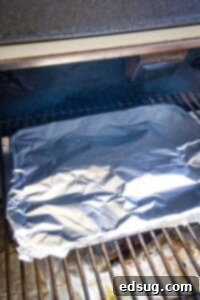 A chuck roast covered with aluminum foil in a pan, on a smoker.