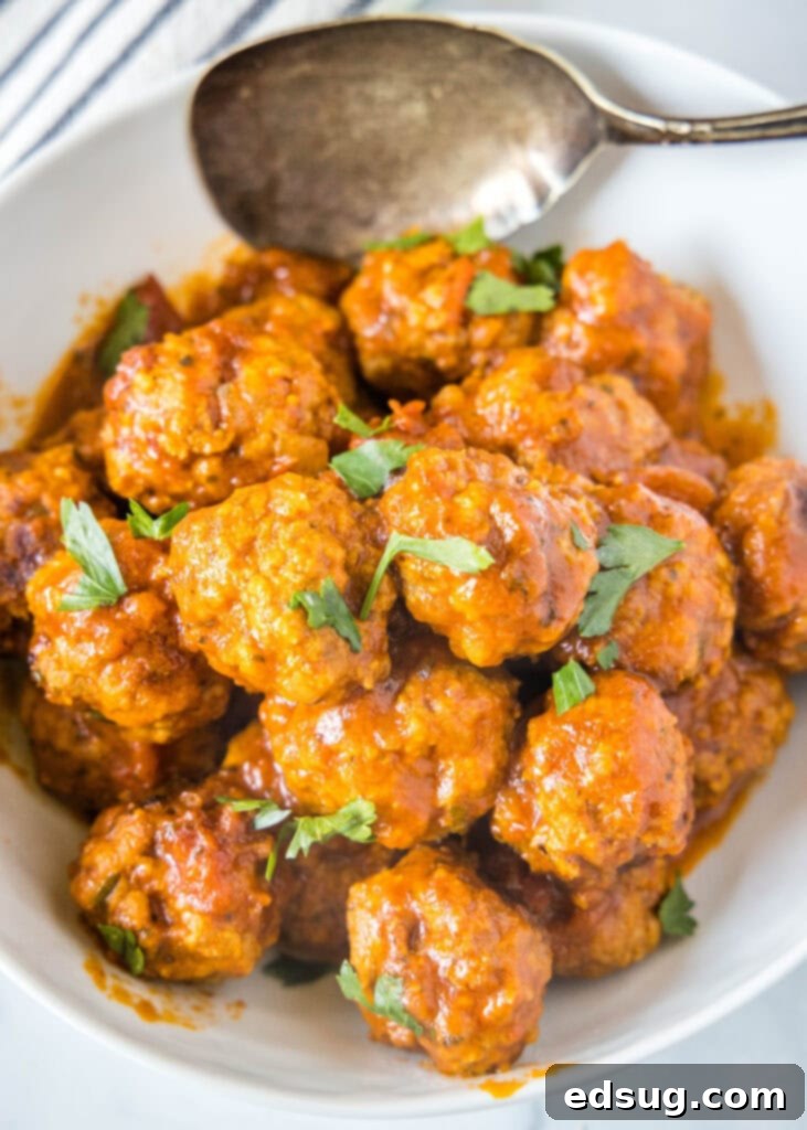 Looking down on a bowl of rich, red marinara sauce filled with perfectly cooked Instant Pot Meatballs, garnished with fresh herbs.