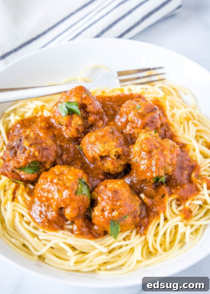 A generous serving of Instant Pot Meatballs in marinara sauce, piled high over a bed of freshly cooked spaghetti, garnished with parsley.