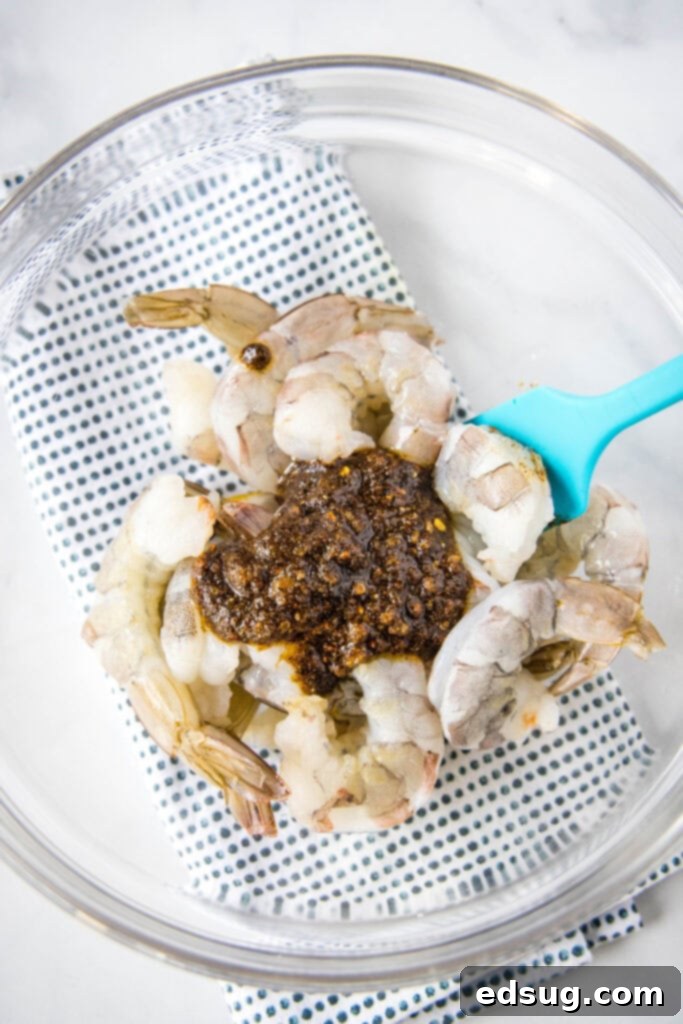 Raw shrimp in a mixing bowl, generously coated with a vibrant spice mixture and olive oil.