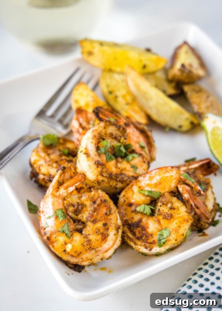 Plated air fryer shrimp alongside roasted potato wedges and a garnish of fresh herbs.