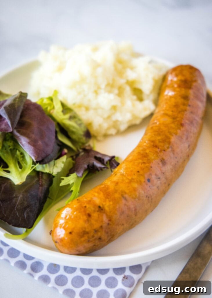 Perfectly cooked air fryer sausage served on a clean white plate alongside a fresh green salad and golden roasted potatoes, creating a balanced and appealing meal presentation.