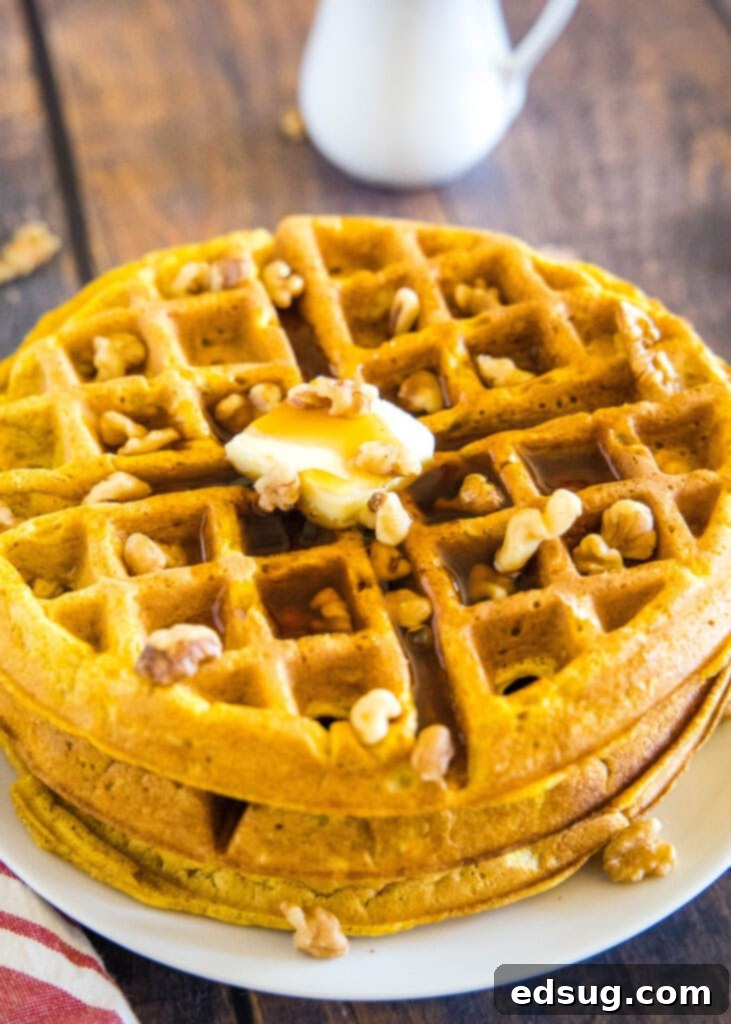 A stack of golden pumpkin waffles adorned with maple syrup and chopped walnuts, ready to be served