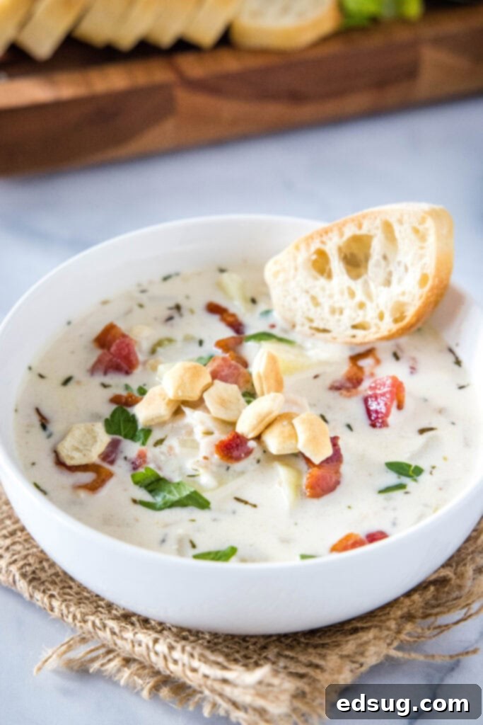 Ultimate Creamy Clam Chowder 2 A hearty bowl of homemade clam chowder garnished with a slice of bread and oyster crackers, ready to be enjoyed.
