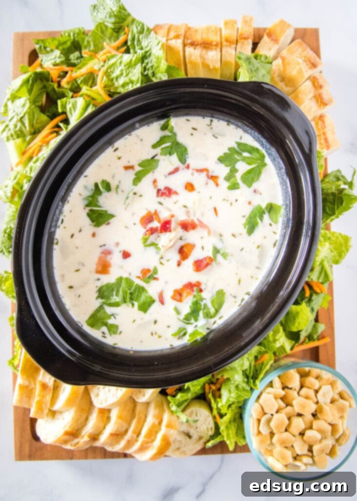 Ultimate Creamy Clam Chowder 4 An elaborate clam chowder board featuring a central pot of chowder surrounded by fresh salad, slices of crusty bread, and crispy oyster crackers.