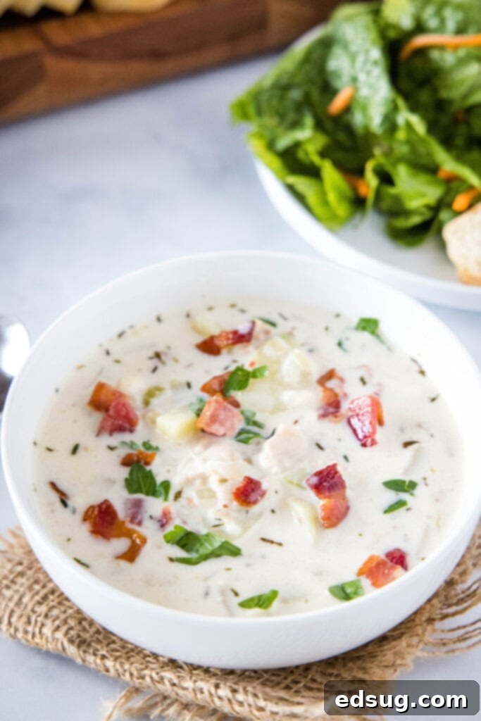 Ultimate Creamy Clam Chowder 6 A close-up of a white bowl of creamy clam chowder, generously topped with crispy bacon bits, showcasing its enticing texture.
