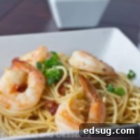 A dish of Speedy Shrimp Pasta, featuring succulent shrimp, bright pasta, and a savory sauce, garnished with fresh herbs and a lemon wedge.