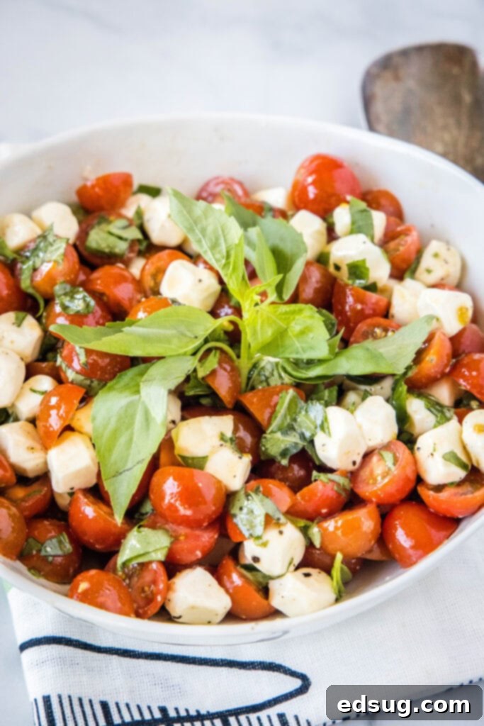 A vibrant bowl of Tomato Mozzarella Salad, showcasing fresh red tomatoes, white mozzarella, and green basil leaves, drizzled with balsamic glaze.
