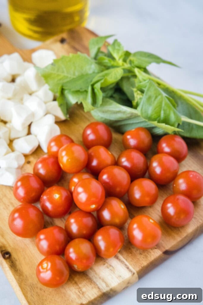 Ingredients for Caprese salad laid out, including cherry tomatoes, mozzarella pearls, and fresh basil.