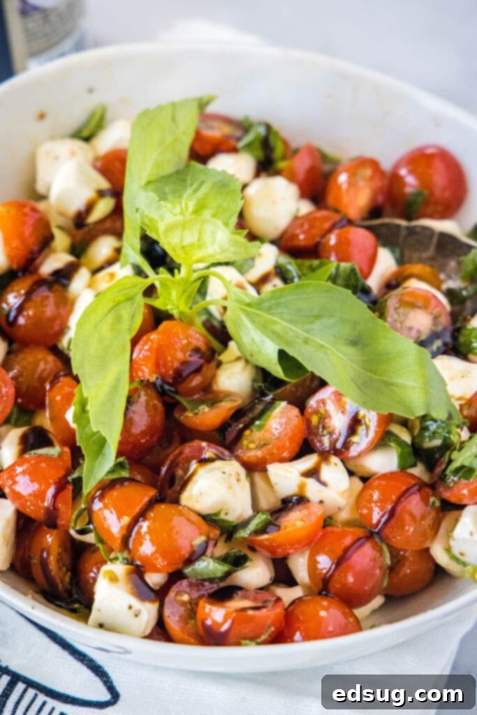 Balsamic glaze being drizzled over a fresh tomato and mozzarella salad in a bowl.