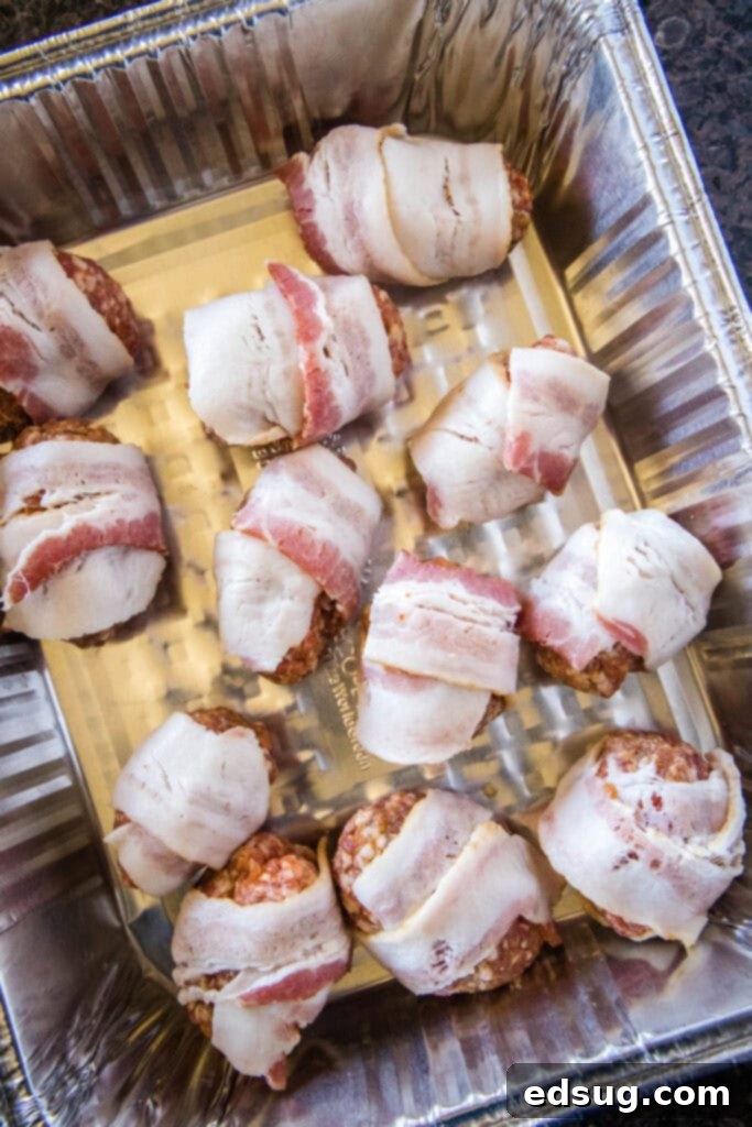 Prepared armadillo eggs, wrapped in sausage and bacon, placed in a metal tray ready for the smoker
