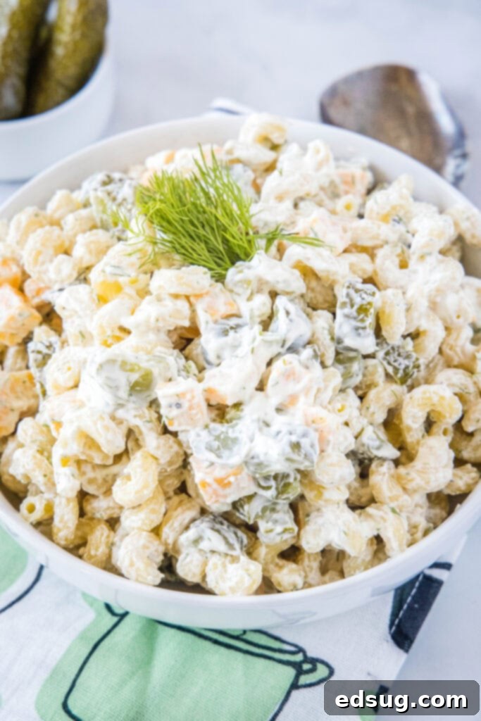 Close up of a white bowl filled with creamy dill pickle pasta salad, garnished with fresh dill.