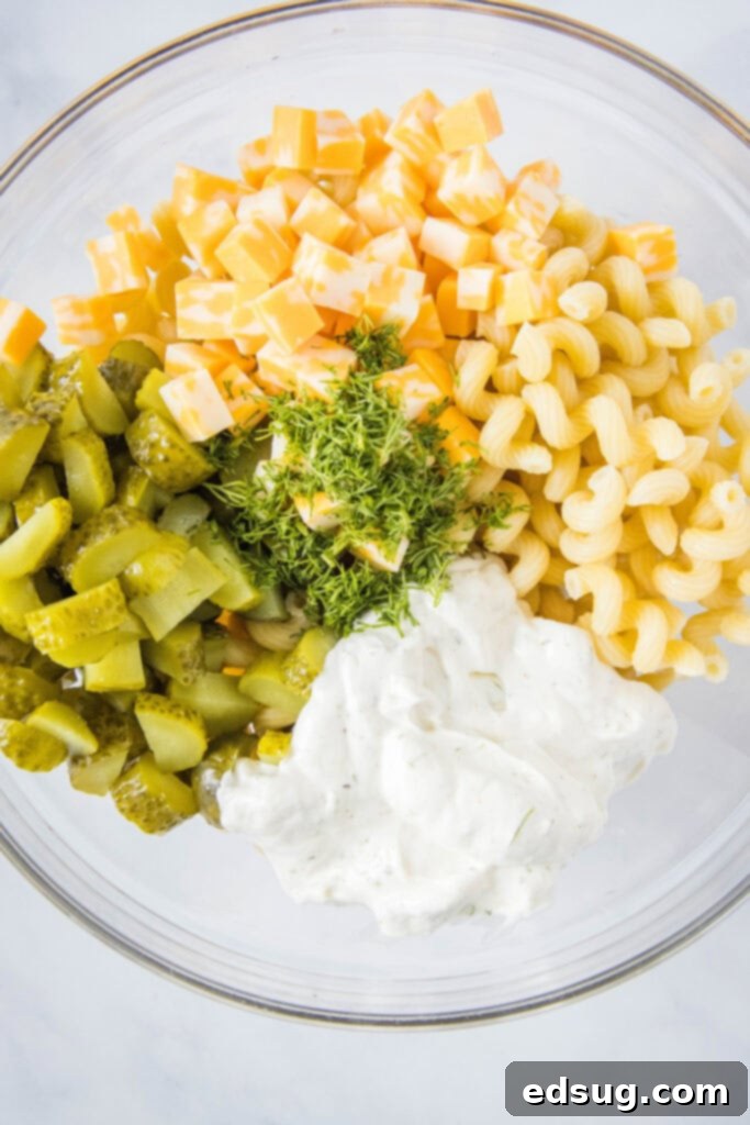 Hands mixing dill pickle pasta salad in a large glass bowl with a spoon.