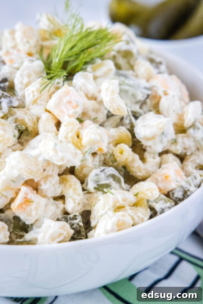 A large white bowl of dill pickle pasta salad with pickles and cheese visible.