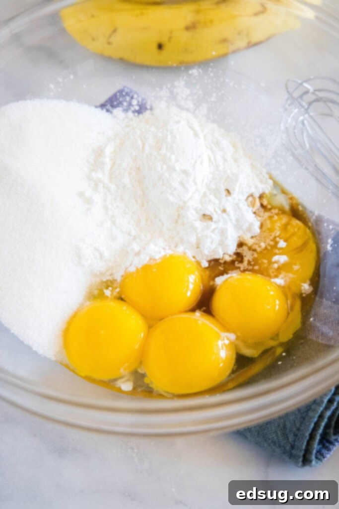 The initial step of mixing ingredients for the rich, decadent, and banana-loaded cream pie filling, as good as anything from a bakery. A bowl with granulated sugar, cornstarch, egg yolks, and vanilla extract being whisked together for the pie filling.