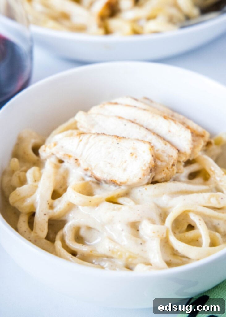 A white bowl with fettuccine Alfredo with chicken on top, garnished with parsley