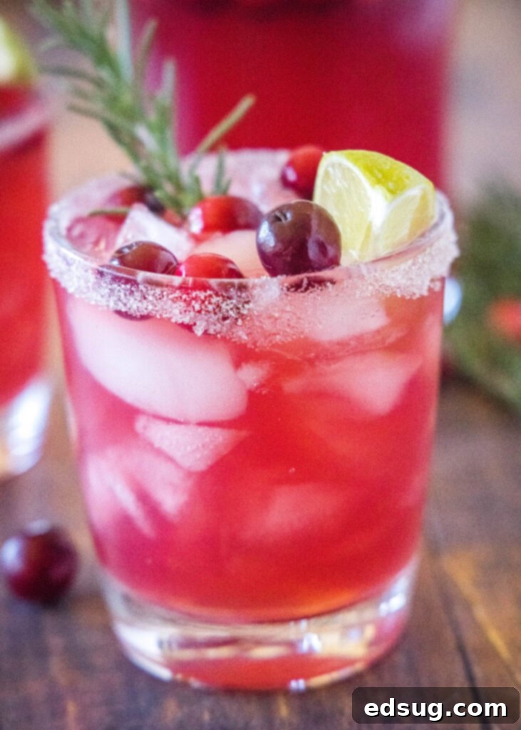 Vibrant Mistletoe Margarita cocktail in a glass, garnished with fresh cranberries and a sprig of rosemary, perfect for holiday parties.