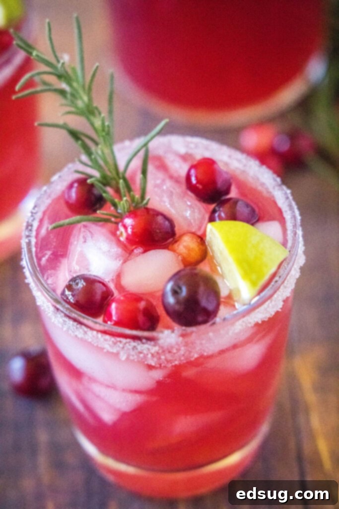 Overhead view of a Mistletoe Margarita in a glass filled with ice, garnished with vibrant fresh cranberries and a fragrant rosemary sprig.