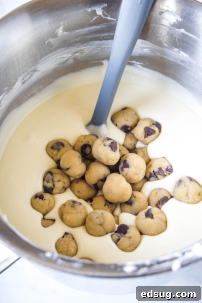 Close-up of cheesecake batter with small, frozen edible cookie dough balls folded in, ready for baking.