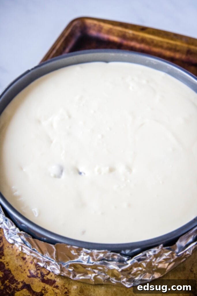An unbaked chocolate chip cookie dough cheesecake in a springform pan on a baking sheet, ready for the oven.