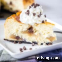 Close up of chocolate chip cookie dough cheesecake on a plate topped with whipped cream, showing the creamy texture and cookie dough pieces.