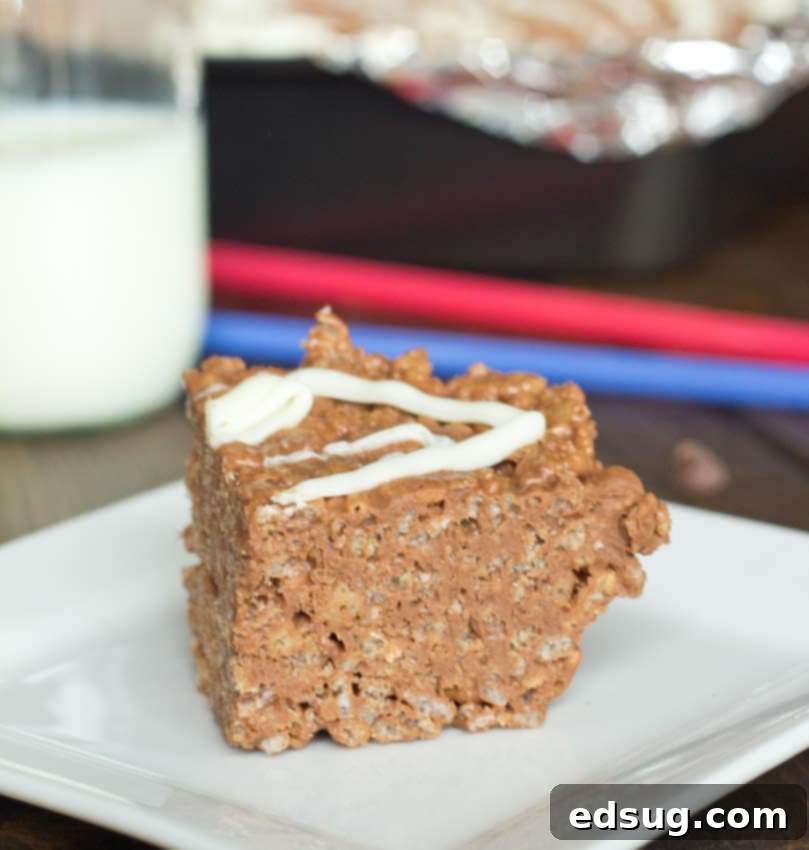 A hand drizzling melted white chocolate over a pan of chocolate peanut butter krispie treats before they set.