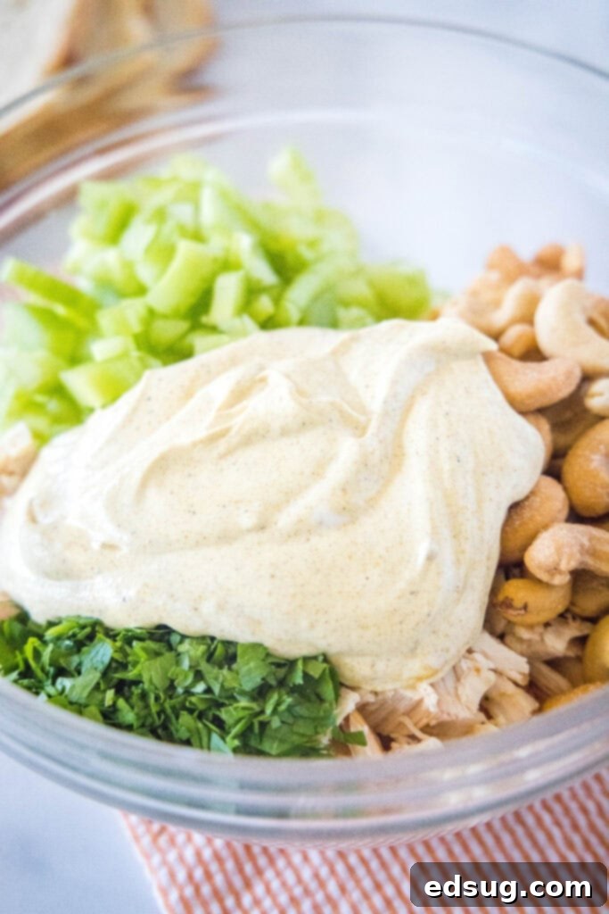Adding creamy curry dressing over the shredded chicken mixture in a large mixing bowl.