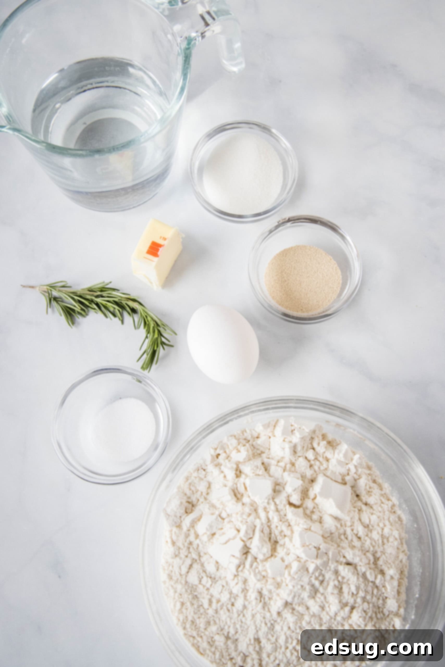 A collection of ingredients for Amish bread, including flour, butter, sugar, yeast, and a bowl of water, neatly arranged on a countertop.