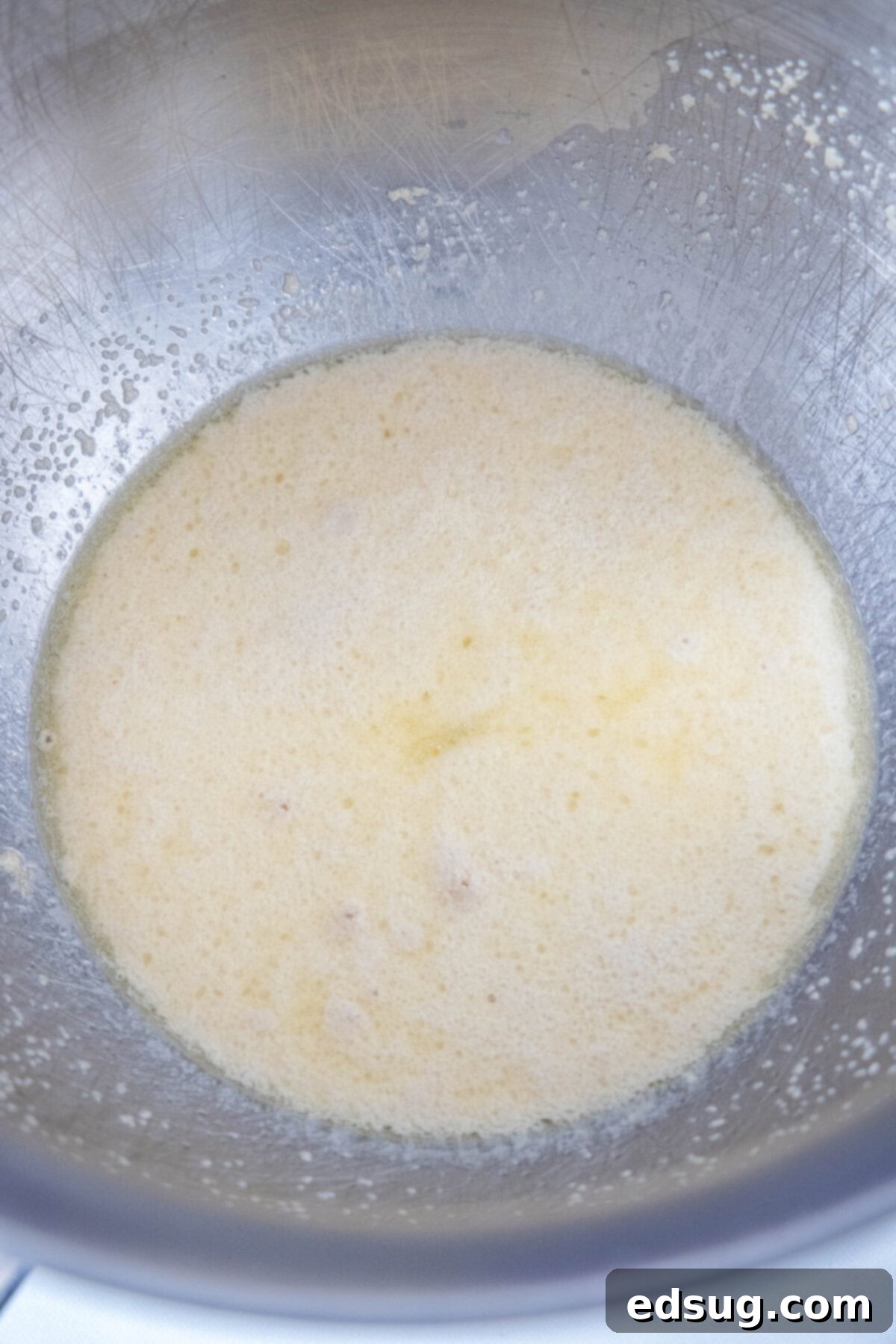 Yeast mixed with sugar and warm water in a metal stand mixer bowl, showing a foamy surface indicating activation.