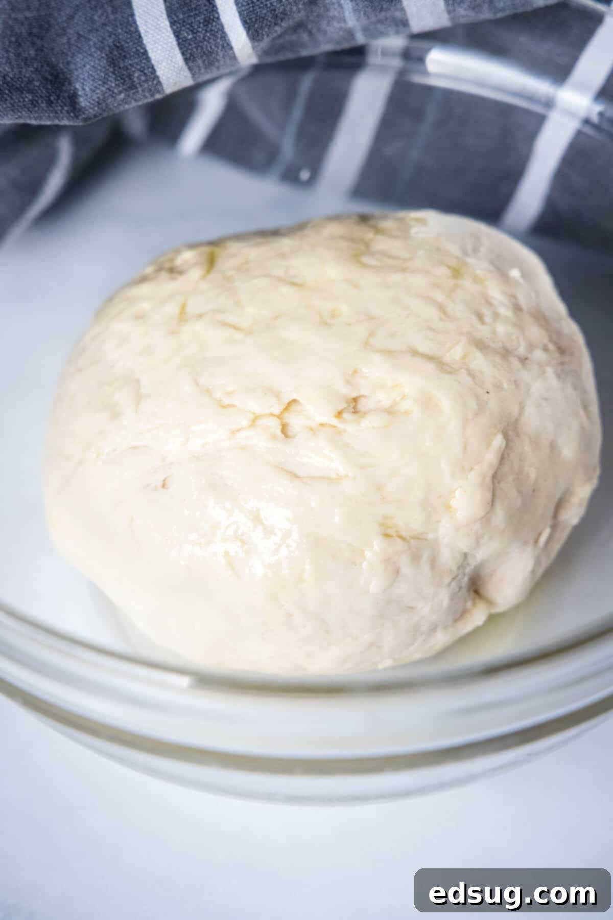 Amish country bread dough forming a cohesive ball in a clear glass mixing bowl, after flour has been added and partially kneaded.