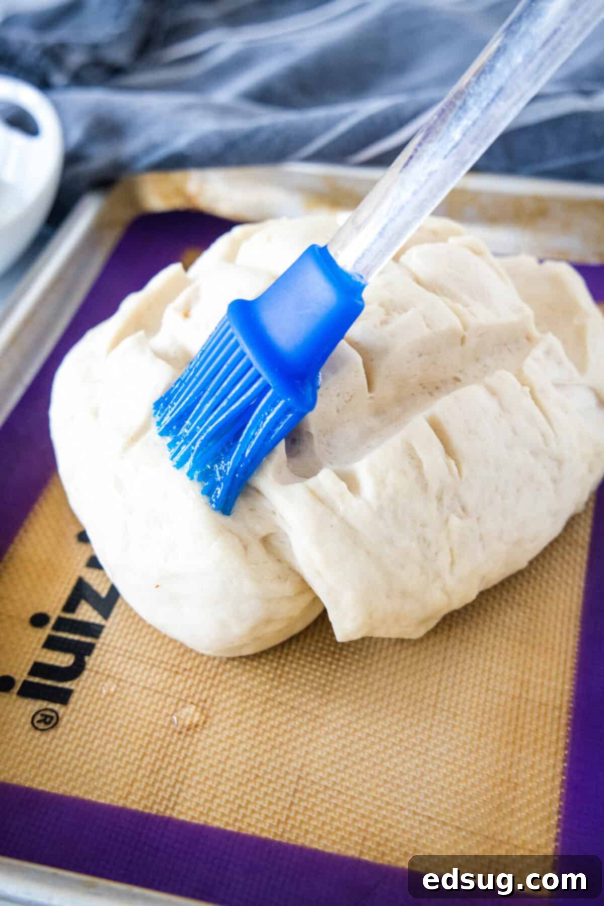 A basting brush carefully applying an egg wash to the scored top of Amish bread dough, preparing it for baking.