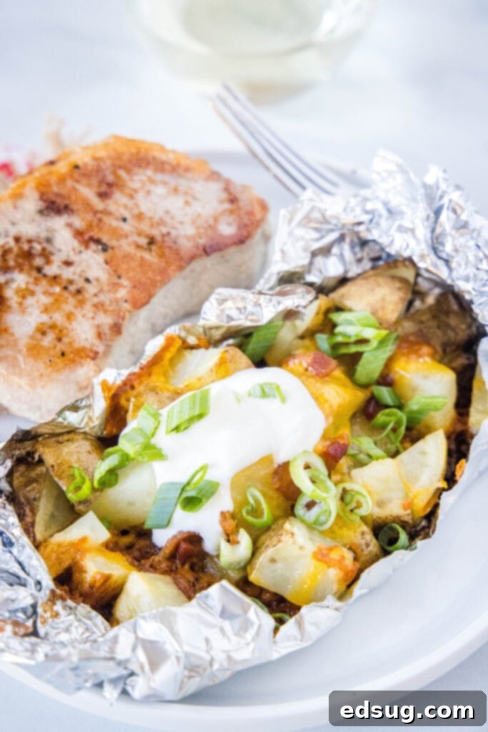 Grilled potato foil pack on a white plate, garnished with fresh chives.