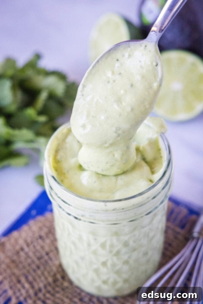 Scooping creamy avocado dressing out of a mason jar, showcasing its smooth, vibrant green texture, ready to be served or added to a fresh salad.