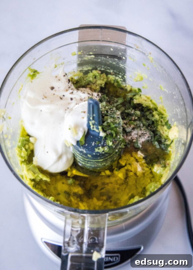 All the fresh ingredients for creamy avocado dressing meticulously placed inside a small food processor, perfectly arranged and ready to be blended into a smooth, luscious mixture.