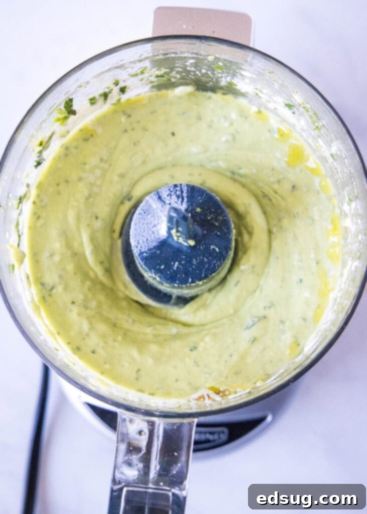Freshly made, smooth avocado dressing sitting in the bowl of a food processor, ready to be transferred to a storage container or drizzled over a delicious meal.