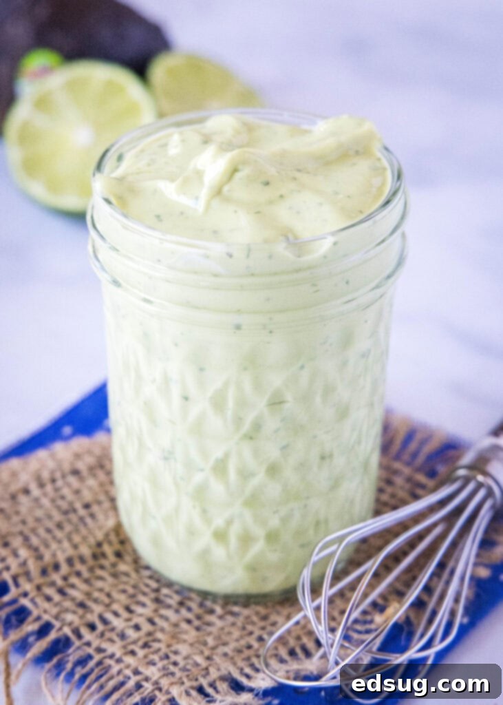 A charming clear glass jar filled with vibrant green creamy avocado dressing, with a small silver whisk casually placed alongside on a rustic wooden surface, ready for use.