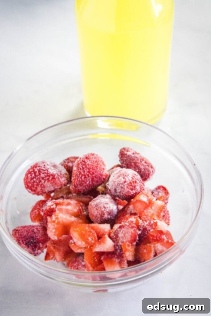 Ingredients for frozen strawberry lemonade laid out: a bag of frozen strawberries, a pitcher of lemonade, and a bowl of sugar.