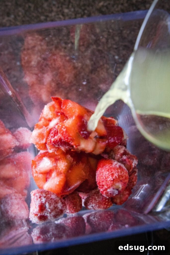 Frozen strawberries being poured into a blender, followed by lemonade being added over them.
