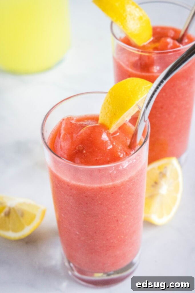 A refreshing glass of frozen strawberry lemonade with a stylish metal straw, sitting on a rustic wooden surface.