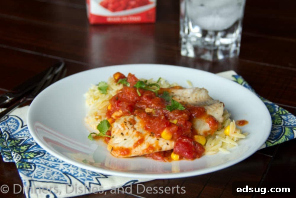 Overhead shot of tilapia with tomatoes and orzo in a serving dish, beautifully arranged and ready to be plated.
