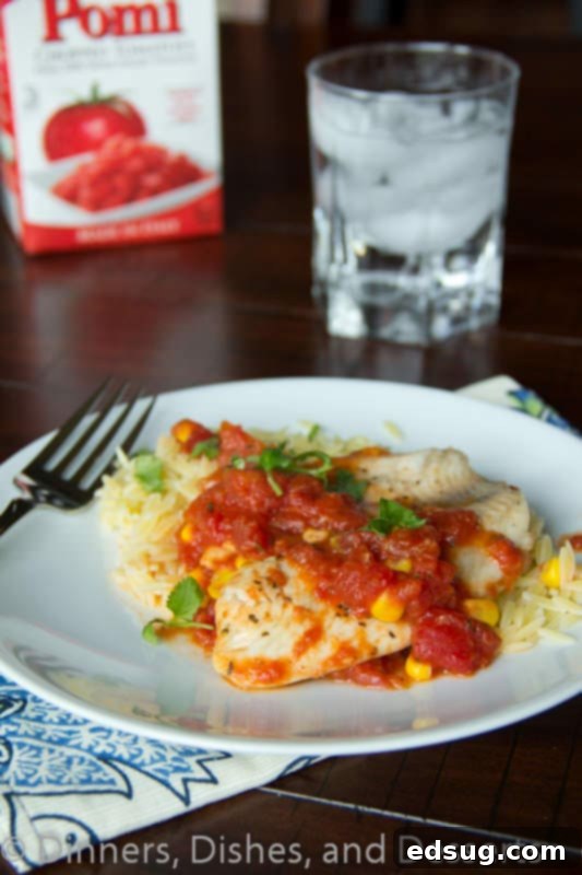 Close-up of a fork taking a bite of tilapia with tomatoes and orzo, showing the flaky fish and saucy pasta.