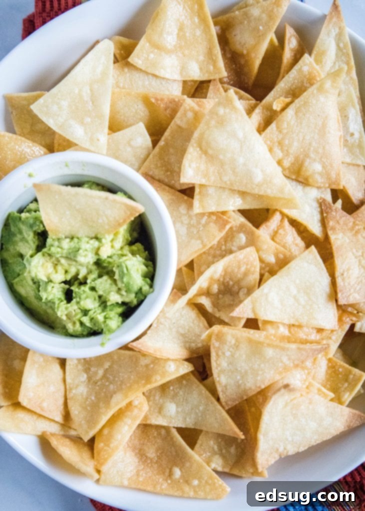overhead view of a bowl of homemade tortilla chips with a serving of guacamole in the background