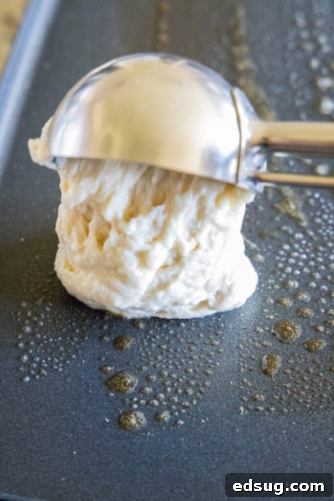 A scoop of rich buttermilk pancake batter being poured onto a hot, buttered griddle, beginning the cooking process for perfectly round pancakes.