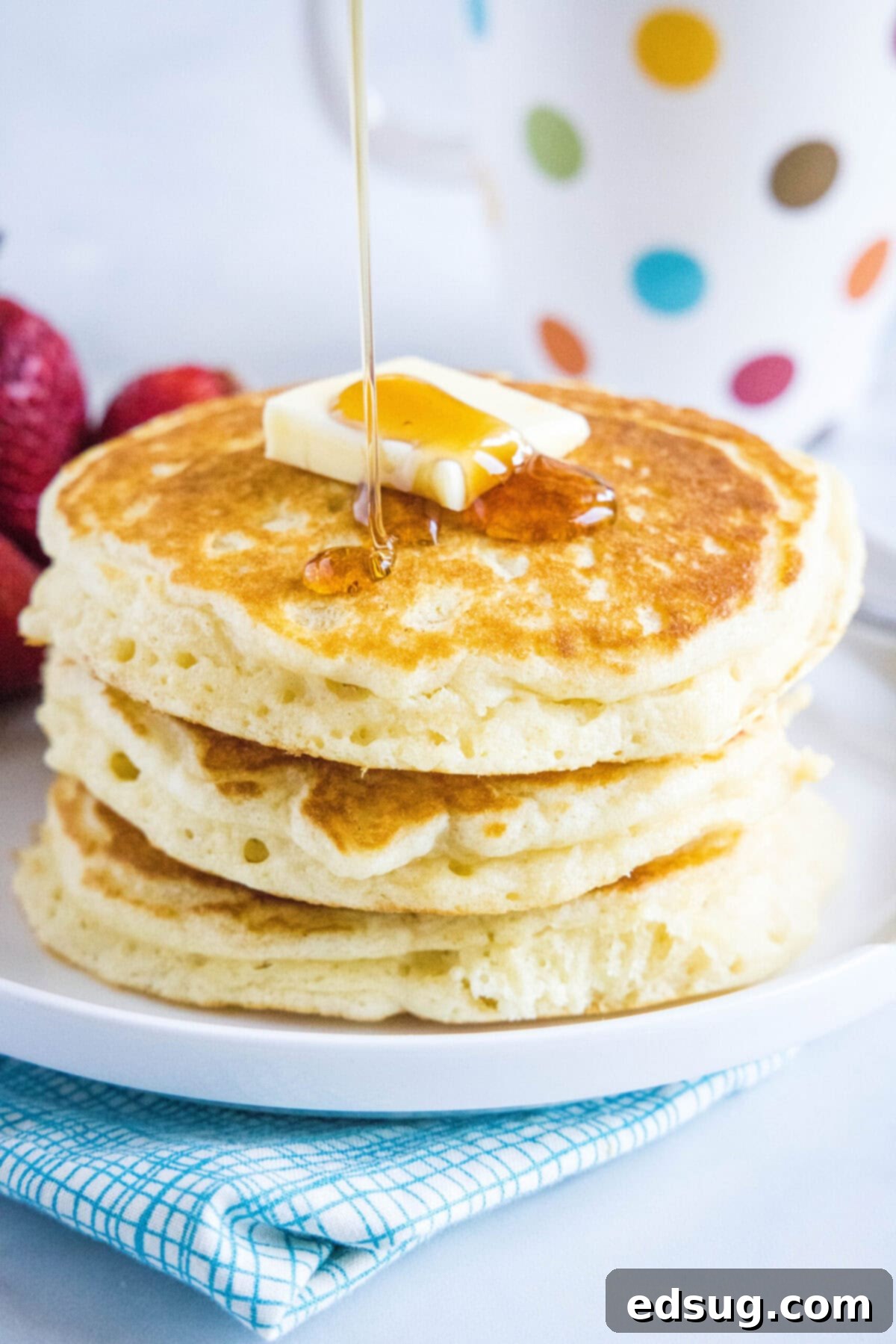 Rich, amber maple syrup being generously poured over a delectable stack of fluffy buttermilk pancakes, perfectly topped with a melting pat of butter, creating an inviting breakfast scene.